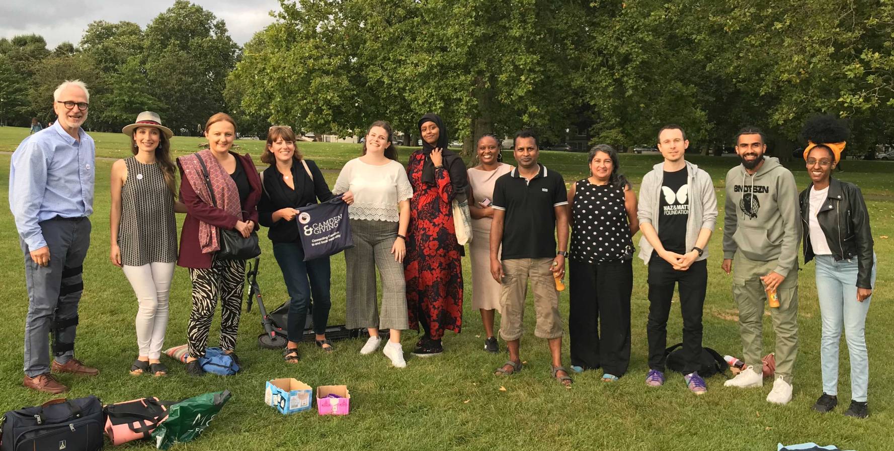 A large group of people stand in a line for a photo, in a park