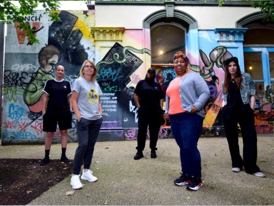 Group shot of young black and white women in front of a colourful painted building