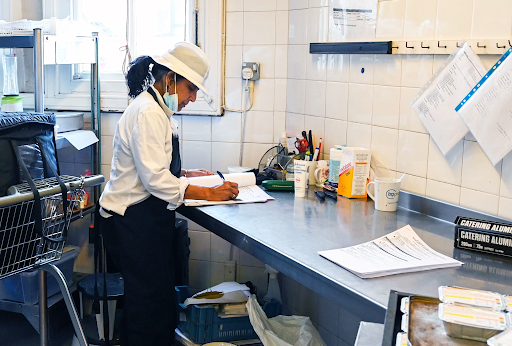 A woman in a chef's uniform filling in a paperwork on the counter of a commercial kitchen