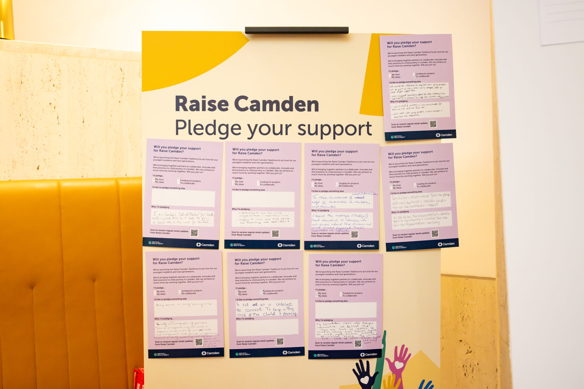 A yellow board reading 'Raise Camden - Pledge your support' holds purple pledge cards with guests' commitments to tackling child poverty written on them.