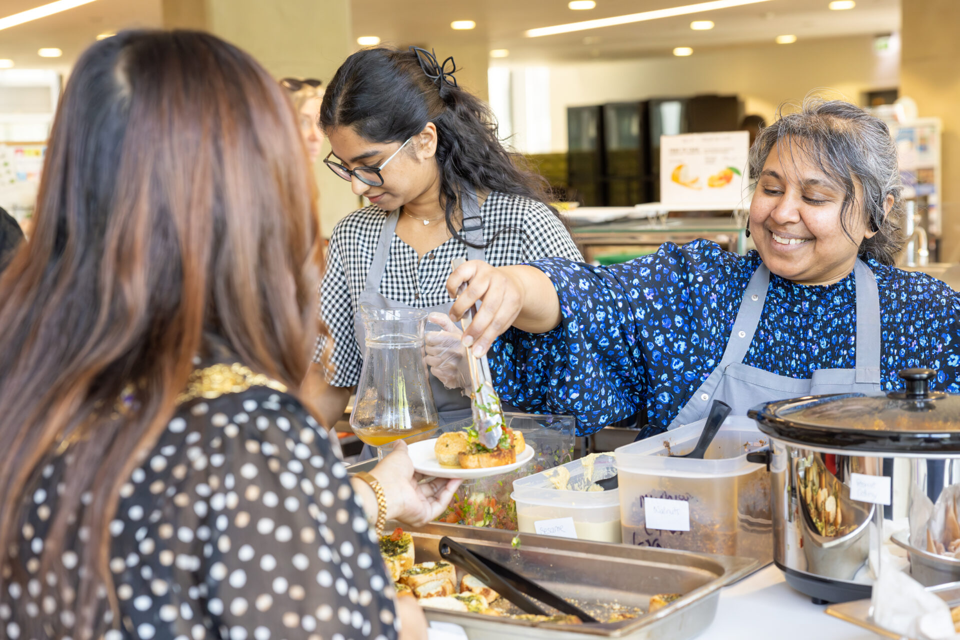 Two individuals serving food to a customer at the community café. One person hands over a plate while another assists in the background.