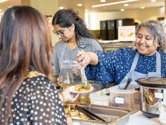 Two individuals serving food to a customer at the community café. One person hands over a plate while another assists in the background.