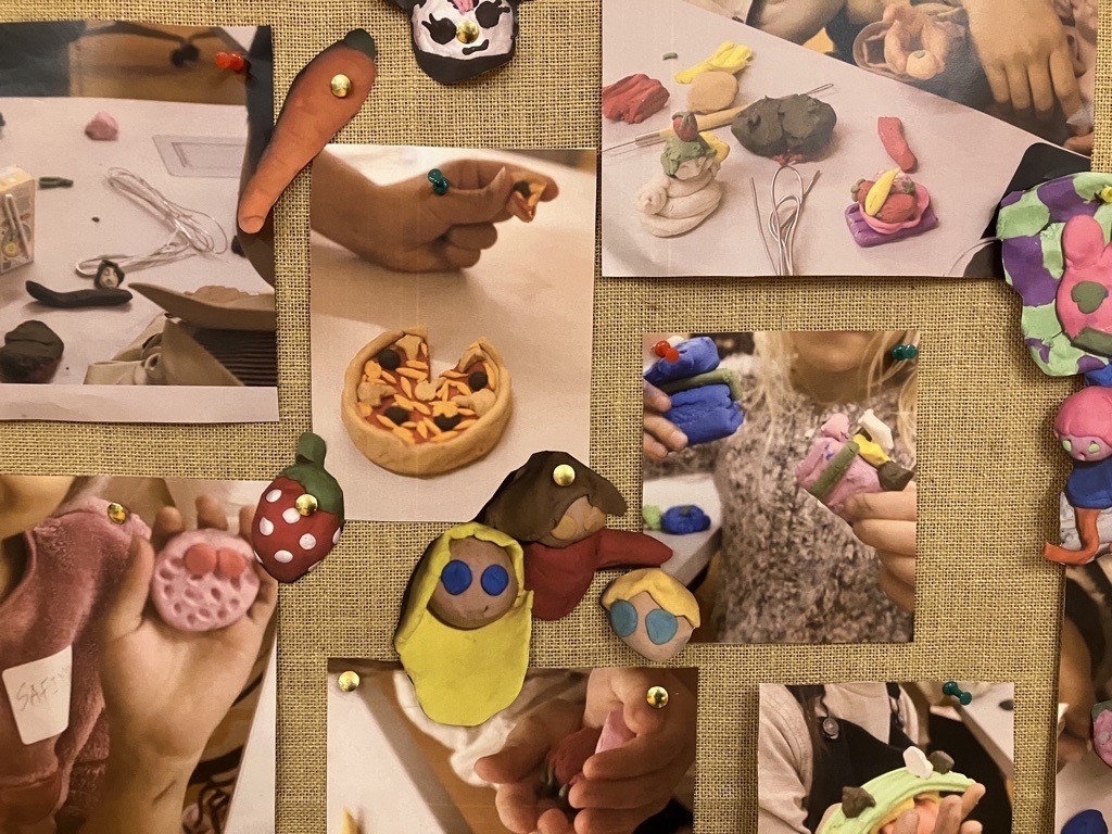 A display board covered with photos of hands making small clay models, surrounded by colourful clay shapes pinned around the images.