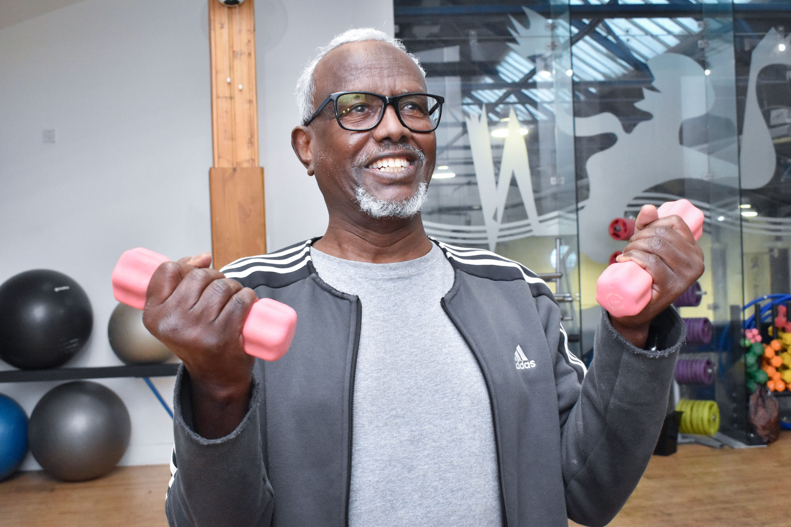 A man wearing glasses is using 2 pink dumbbells to exercise